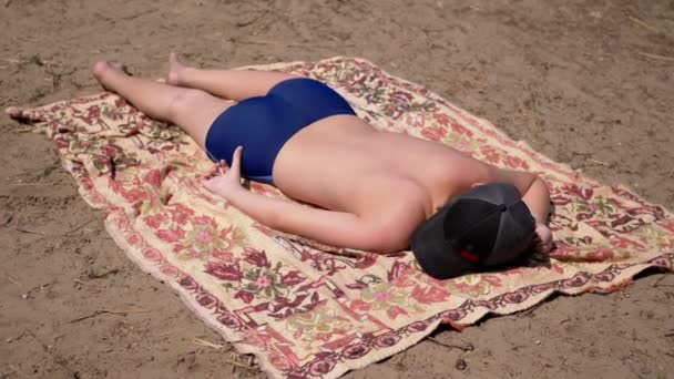 少年日光浴 寝そべって 太陽の砂の上のカバーレットのビーチで寝る バックビュー 自然の中で休息 暖かい日差しを楽しむ水泳トランクで幸せな日焼けした裸の子供を眠る — ストック動画