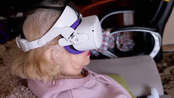 使用3D虚拟现实眼镜坐在沙发上的令人惊讶的女人 年长的游戏女性看到一个三维图像 一个戴Vr眼镜的视频 并旋转头部 人工智能 — 图库视频影像