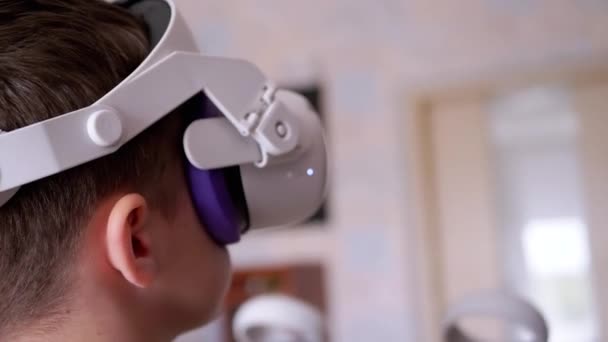ゲームコントローラー付き3Dメガネのティーンエイジャーは防音室でプレイします 白いヘルメットの少年は ヘッドセットVrテスターで手を動かし 部屋を歩いています 仮想現実 装置だ 人工知能 — ストック動画