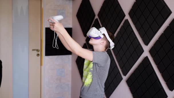 与游戏控制器一起玩3D眼镜的青少年在一个隔音室内玩耍 戴白色头盔的男孩带着耳机Vr测试仪走在房间里 虚拟现实 人工智能 — 图库视频影像