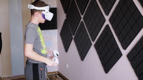 ゲームコントローラー付き3Dメガネのティーンエイジャーは防音室でプレイします 白いヘルメットの少年は ヘッドセットVrテスターで手を動かし 部屋を歩いています 仮想現実 装置だ 人工知能 — ストック動画