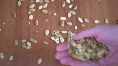 Masadaki Kadın Eller 'den bir sürü ham kabak tohumu düştü. Atılmış yeşil balkabağı çekirdekleri parmaklarının arasından bir masanın üzerindeki tohum yığınına düşer. Dağınık taneler. Doğal, besleyici, sağlıklı ürün..