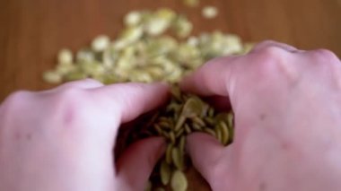Masadaki Kadın Eller 'den bir sürü ham kabak tohumu düştü. Atılmış yeşil balkabağı çekirdekleri parmaklarının arasından bulanık bir zemindeki tohum yığınına düşer. Doğal, besleyici, sağlıklı ürün..