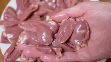 Dişi El, taze çiğ tavuk kalplerini tabağa koydu. Offal. Bir sürü parlak kırmızı tavuk kalbi var, ikiye bölünmüş. Beslenme eti. İkinci sınıfın yan ürünleri. Fakirler için ucuz yemek..