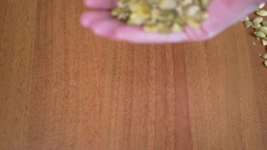 Masadaki Kadın Eller 'den bir sürü ham kabak tohumu düştü. Atılmış yeşil balkabağı çekirdekleri parmaklarının arasından bir masanın üzerindeki tohum yığınına düşer. Dağınık taneler. Doğal, besleyici, sağlıklı ürün..