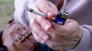 Elinde sigara tutan kadın ve doğada güneşin altında oturan bir çakmak. Dışarıda sigara içen bir kadın, park eder. Sigara içiyorum. Kötü alışkanlık. Bağımlılık. Sağlıksız yaşam tarzları. Stres yüzünden. Dinleniyor.