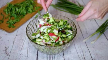 Sebze salatası, salatalık, salatalık, yeşillik ve sebzeyle karıştırılan eller. Yakın plan. Renkli yeşil soğan, maydanoz, turp ve salatalık sebzesi karışımı, yağ. Vejetaryen diyeti. Sağlıklı yemek..