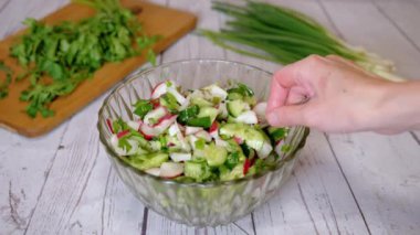 Sebze salatası, salatalık, salatalık, yeşillik ve sebzeyle karıştırılan eller. Yakın plan. Renkli yeşil soğan, maydanoz, turp ve salatalık sebzesi karışımı, yağ. Vejetaryen diyeti. Sağlıklı yemek..