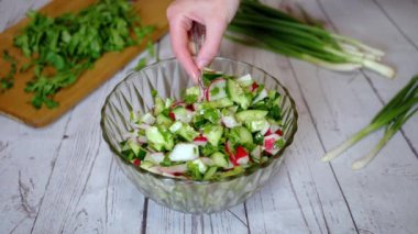 Sebze salatası, salatalık, salatalık, yeşillik ve sebzeyle karıştırılan eller. Yakın plan. Renkli yeşil soğan, maydanoz, turp ve salatalık sebzesi karışımı, yağ. Vejetaryen diyeti. Sağlıklı yemek..