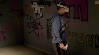 UKRAINE, KAMENSKOE, 2022: 3 boyutlu Gözlüklü Genç Sanal Gerçeklik Odasında Oynuyor. Mutlu çocuk karanlık odanın yanından geçiyor, VR test cihazını beyaz kulaklıkla hareket ettiriyor ve oynuyor. Cihaz. Uygulama.