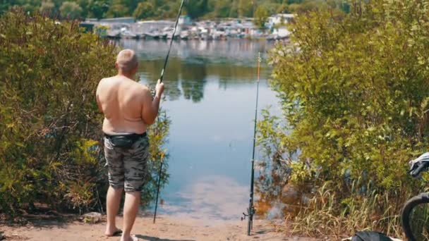 渔夫用螺旋桨把捕获的鱼拖出水面 后视镜男人赤身裸体和两根杆子在夕阳西下的一个池塘里钓鱼 — 图库视频影像