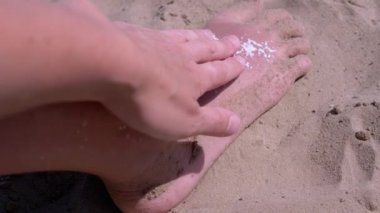 Kadın eli, bronzlaşmış kırmızı bacak derisine güneş kremi sürüp sürtünüyor. Güneş yanığı kremi. Güvenli bronzlaşma ve plajda güneşli bir yaz gününde bir çocuğun cilt bakımı. Gün batımında güneş ışığı. Dinlen, hafta sonu.