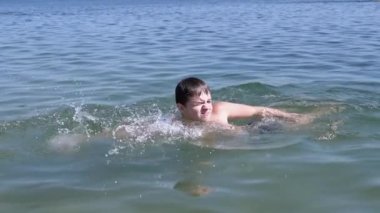 Happy Child Swimming, Diving, Holds Breath Underwater on Blue Water in Sunrays. A boy learns to swim freestyle on beach. Sports training. Health. Rest, recuperation, summer family vacation. Lifestyle.