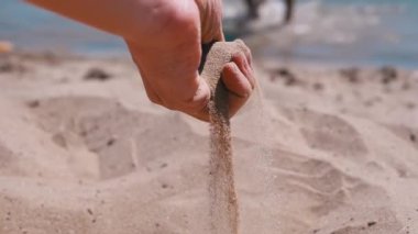 Female Hand Pours Sand Through Fingers on the Beach in the Rays of Sunlight. Fine grains of sand slowly fall on the hot golden sand in the sun glare at sunset. Rest on the sea coast, a seaside resort.