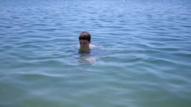 Mutlu Genç Su Sıçratma, Dalma ve Sahildeki Okyanus Suyu 'nda Eğlenme. Çocuk yüzmeyi, suyun altına dalmayı öğreniyor. Biraz su, zevk, neşe. Aile dinlenmesi, iyileşme, yaz tatili..