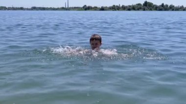 Üzgün Çocuk Yüzme, Denizde Güneş Sahilinde Su Sıçratma. Çocuk suda oynuyor, dalgalar yaratıyor, ellerle su sıçratıyor. Aile dinlenmesi, dinlenme, yaz tatili. Deniz tatil köyü. Hafta sonu. Yaz zamanı..