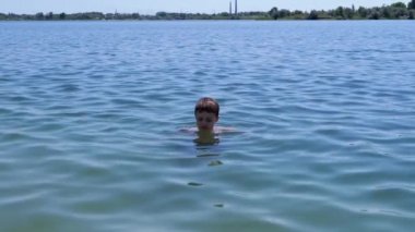 Happy Boy Swimming in Water, Enjoys the Rest of the Sea in Rays of Sunlight. A sad child bathes in the blue sea at sunset. Family rest, recreation, summer vacation. Sea resort. Weekend. Summertime.