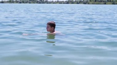 Suda Yüzen Mutlu Çocuk, Güneş Işığıyla Denizin Geri Kalan kısmının tadını çıkarıyor. Üzgün bir çocuk gün batımında mavi denizde yıkanır. Aile dinlenmesi, dinlenme, yaz tatili. Deniz tatil köyü. Hafta sonu. Yaz zamanı..