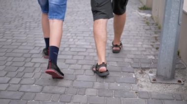 UKRAINE, KAMENSKOE, 2022: Baba ve Oğul 'un Bacakları Yeşil Çimen yakınlarındaki Park' ta Kaldırımda Yürüyor. Yakın plan. Yavaş çekim. İki kişi, bir erkek ve bir genç sokakta birlikte yürüyorlar..