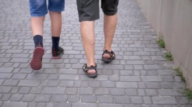 UKRAINE, KAMENSKOE, 2022: Baba ve Oğul 'un Bacakları Yeşil Çimen yakınlarındaki Park' ta Kaldırımda Yürüyor. Yakın plan. Yavaş çekim. İki kişi, bir erkek ve bir genç sokakta birlikte yürüyorlar..