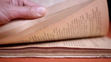 Female Fingers Leafing Through Pages of Old Shabby Book on a Black Background. Reading. Rough papyrus paper on a thick antique book from yesteryear. Orange color. Education. Knowledge. Mystic.