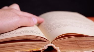 Woman Reading a Book by Candlelight in a Dark Room, Follows a Text with Finger. Close up. Girl runs finger over old yellow page of an old book. Mysterious atmosphere. Night. Black background.