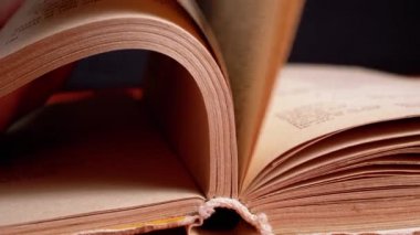 Female Fingers Leafing Through Pages of Old Shabby Book on a Black Background. Reading. Rough papyrus paper on a thick antique book from yesteryear. Orange color. Education. Knowledge. Mystic.
