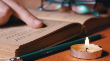 Woman Reading a Book by Candlelight in a Dark Room, Follows a Text with a Finger. Close up. Girl runs finger over old yellow page of an ancient, antique book. Mysterious, mystical atmosphere. Night.