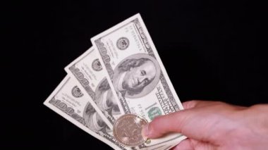Hand Holding One Silver Bitcoin Coin and 100 Dollar Bills on Black Background. Concept of buying, investing in virtual cryptocurrency. Wealth. E-money. Virtual currency. Electronic money exchange.
