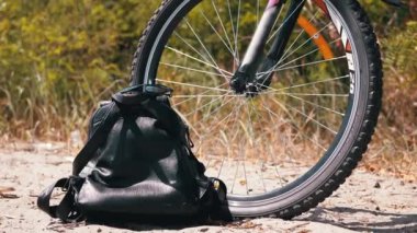 Sports Bike Standing in Forest on the Sand along with a Backpack and Sunglasses. Close-up of front wheel of a spoked bicycle. Concept sports, recreation, tourism, weekend, active lifestyle. No people.