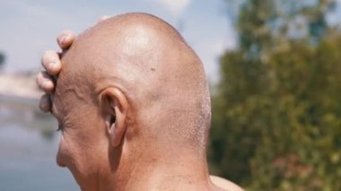 Pensive Bald Male Thinks, Dreams in Nature, Stroking Head with Hand Outdoors. Guy scratches forehead, dreams, looks thoughtfully into distance, thinks about problems in forest in the rays of sunlight.