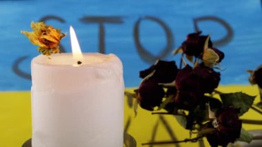Burning Candle with Withered Dry Flowers against Background of Flag of Ukraine. Inscription Stop the war on the yellow-blue flag. Memory of the victims of war, soldiers who died in battle for Ukraine.
