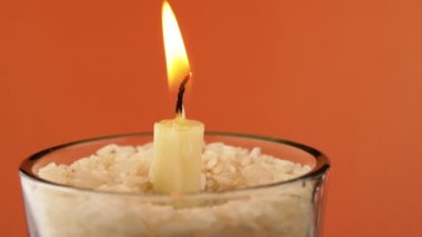 Rotating Burning Candle with a Bright Flame on an Isolated Orange Background. Candle in glass with rice. Concept of memory, ritual, celebration. Abstract, texture, colors. Slow-motion. Close-up.