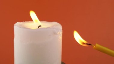Blowing Out Flame Two Burning Church Candles on a Orange Background. Extinguished candles in smoke on an isolated colour background. Clouds of smoke, fog. Concept of memory, ritual, celebration. 4K.