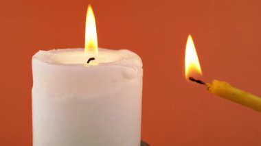 İzole edilmiş turuncu bir arka planda parlak bir alevle yanan iki mum. Elinde sarı bir kilise mumu tutuyordu. Hafıza kavramı, ritüel, kutlama. Soyut arkaplan, doku, renk. Yakın plan..