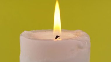 İzole edilmiş sarı arka planda parlak bir alevle yanan beyaz mum. Parlak, sarı, sakin ateş. Hafıza kavramı, ritüel, kutlama. Soyut arkaplan, doku, renk. Yavaş çekim. Yakın plan..