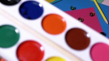 Kadın Elleri Resim Masası 'na Bir Palet Suluboya Koyuyor. Renkli renkli renkli karton kalemlerin arka planında çok renkli boyalar, kağıt. İş yeri hazırlığı.