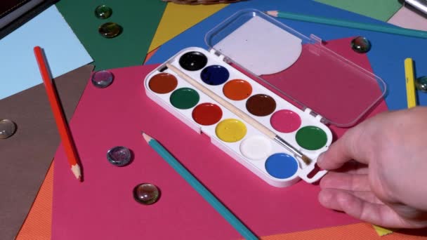 女性的手从画台上移除了一组水彩画 一套色彩斑斓的彩绘画 背景是色彩斑斓的彩色铅笔 工作场所清洁 — 图库视频影像