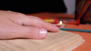 Woman Reading a Book by Candlelight in a Dark Room, Follows a Text with a Finger. Close up. Girl runs finger over old yellow page of an ancient, antique book. Mysterious, mystical atmosphere. Night.