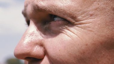 Close-up of a Male Face with Deep Wrinkles Around Eyes Looking at the Sun. A mature bald man thinks about life, looking into the distance at the sky, nature, landscape. Pensive look. Part of the body.