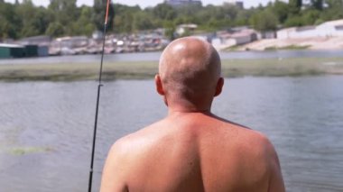 Angler Standing on Riverbank, Catching Fish, Looking into the Distance on Sunset. Back view of a bald man enjoying a fishing trip. Leisure, hobby, lifestyle. Nature, summer landscape. Weekend.