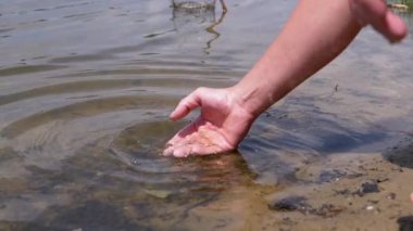 Male Hand Splashing in the Water, playing, creating Splashes in Sun at Sunset. Fingers touching surface of water. Drops are reflected in bright rays of sunlight. Concept of travel, enjoying nature.