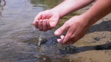 Male Washing Hands in Water on the River Bank in the Rays of the Sun at Sunset. Tourist refreshes himself, rinsing hands at a natural source, a reservoir of river, lake. Vacation, lifestyle concept.