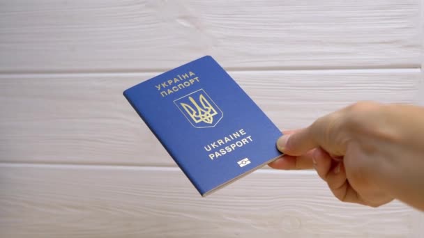 白い背景にウクライナの青い生体パスポートを保持する女性の手 ウクライナのパスポートに記載されています 女の子は海外旅行のための受信した国際文書を示しています — ストック動画