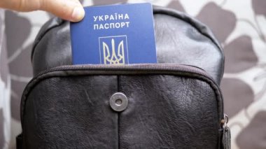 Ukrayna 'nın biyometrik pasaportunu Kara Sırt Çantası' nın cebine koyuyorum. Ukraynaca yazı: Ukrayna pasaportu. Mültecilerin, göçmenlerin yurt dışına çıkışı. Savaş, seyahat, tatil kavramı.