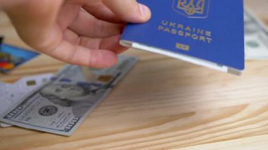 Tahta Masaya 100 Dolarlık banknotla Ukrayna Biyometrik Pasaportu Veriliyor. Dağınık para, masada plastik kartlar. Mültecilerin, göçmenlerin yurt dışına çıkışı. Savaş, seyahat, seyahat, Rus saldırısı.