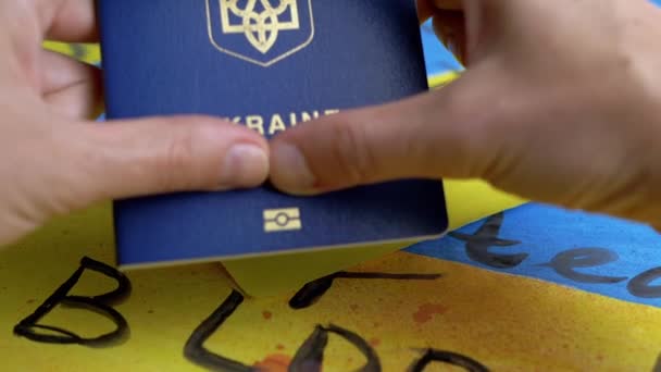 手握心形的手在背景旗上持有乌克兰生物识别护照 乌克兰护照的登记 绘制乌克兰蓝色和黄色的国旗 上面印有停止战争的信息 — 图库视频影像