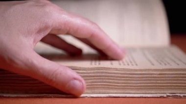 Female Fingers Leafing Through Pages of Old Shabby Book on a Black Background. Reading. Rough papyrus paper on a thick antique book from yesteryear. Orange color. Education. Knowledge. Mystic.