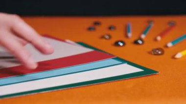 Female Hands Laying Multicolored Sheets of Cardboard on an Orange Background. Preparation of colored paper for the lesson. Learning colors, shapes for preschool kids. Rainbow. School. Education.