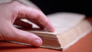 Female Fingers Leafing Through Pages of Old Shabby Book on a Black Background. Reading. Rough papyrus paper on a thick antique book from yesteryear. Orange color. Education. Knowledge. Mystic.